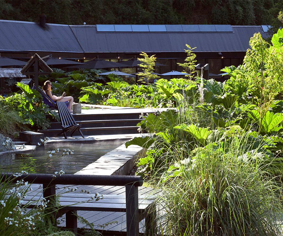 Persona descansando a pasos de una piscina de agua termal rodeada de plantas en Termas del Sol
